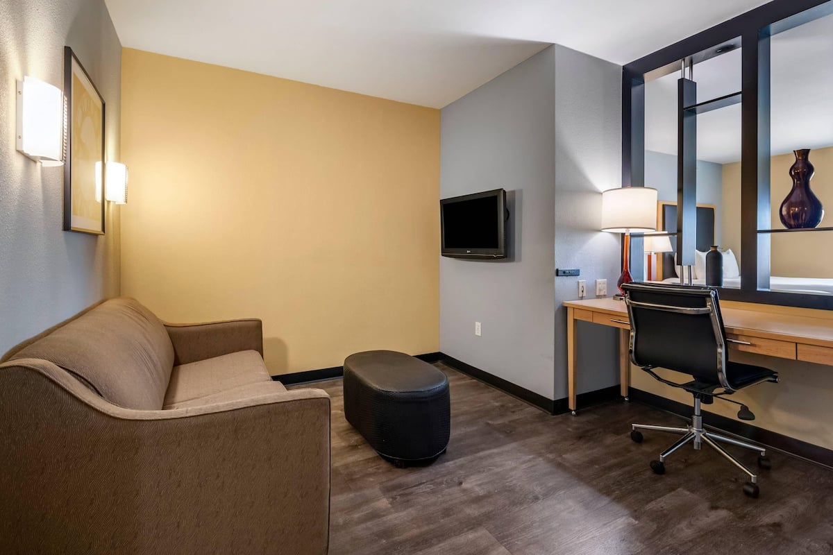 Una habitación de hotel con sofá, escritorio, silla, televisor y lámpara.