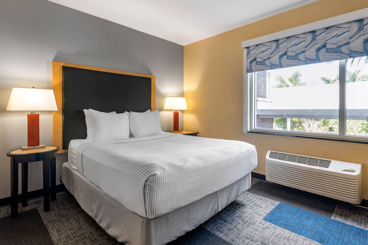 Habitación de hotel con una cama grande, dos mesitas de noche con lámparas, una ventana con vistas y aire acondicionado instalado.