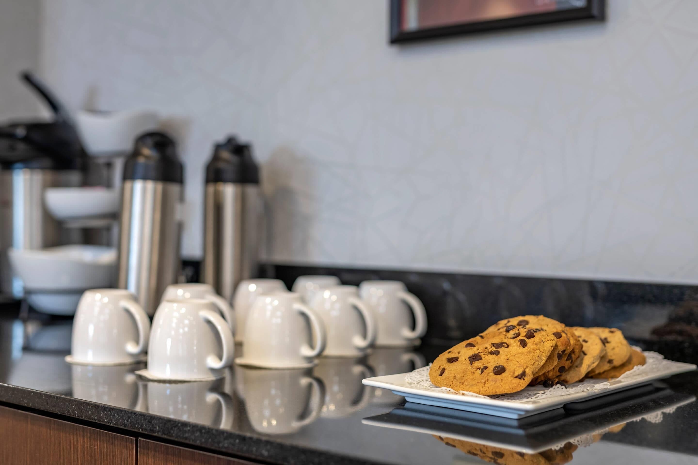 Una encimera de cocina con un plato de galletas y varias tazas blancas.