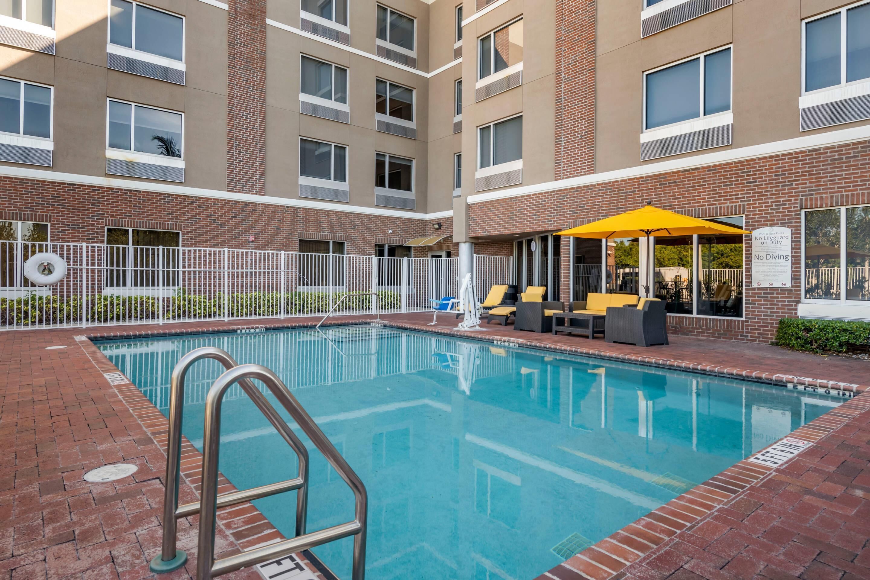 A swimming pool with a white fence, yellow umbrellas, and lounge chairs.