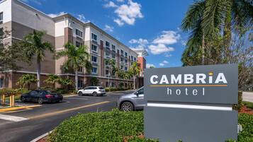 Un letrero de hotel con la inscripción 'CAMBRIA hotel', rodeado de follaje y palmeras.
