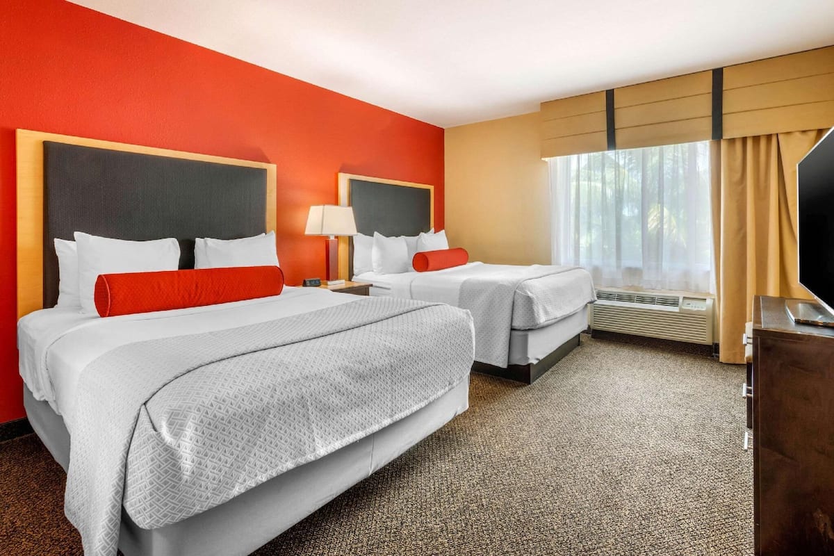 Habitación de hotel con dos camas, televisión y ventana con cortinas.