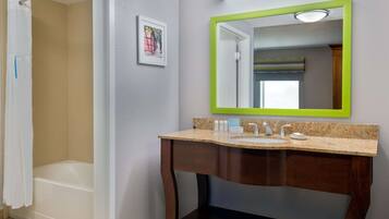 A bathroom with a shower, a sink with a green-framed mirror, and a framed picture on the wall.