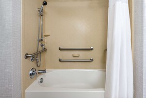 Un baño con bañera, barras de apoyo y cabezal de ducha.
