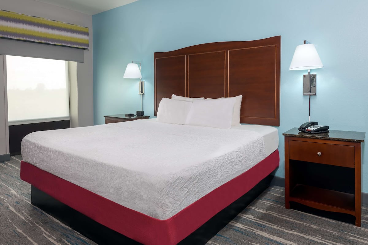 A hotel room with a large bed, two bedside lamps, a nightstand with a phone, and a window with blinds.