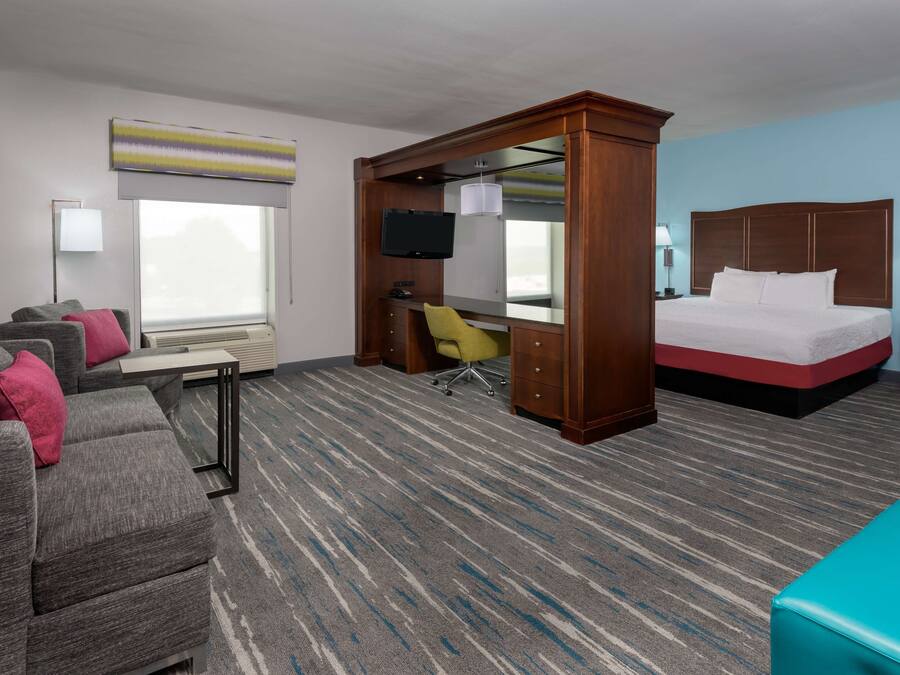 A hotel room with a bed, a desk with a chair, a sofa, a TV, and a window.