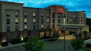 Un hotel moderno con fachada de piedra, múltiples ventanas y un letrero de Hampton Inn & Suites.