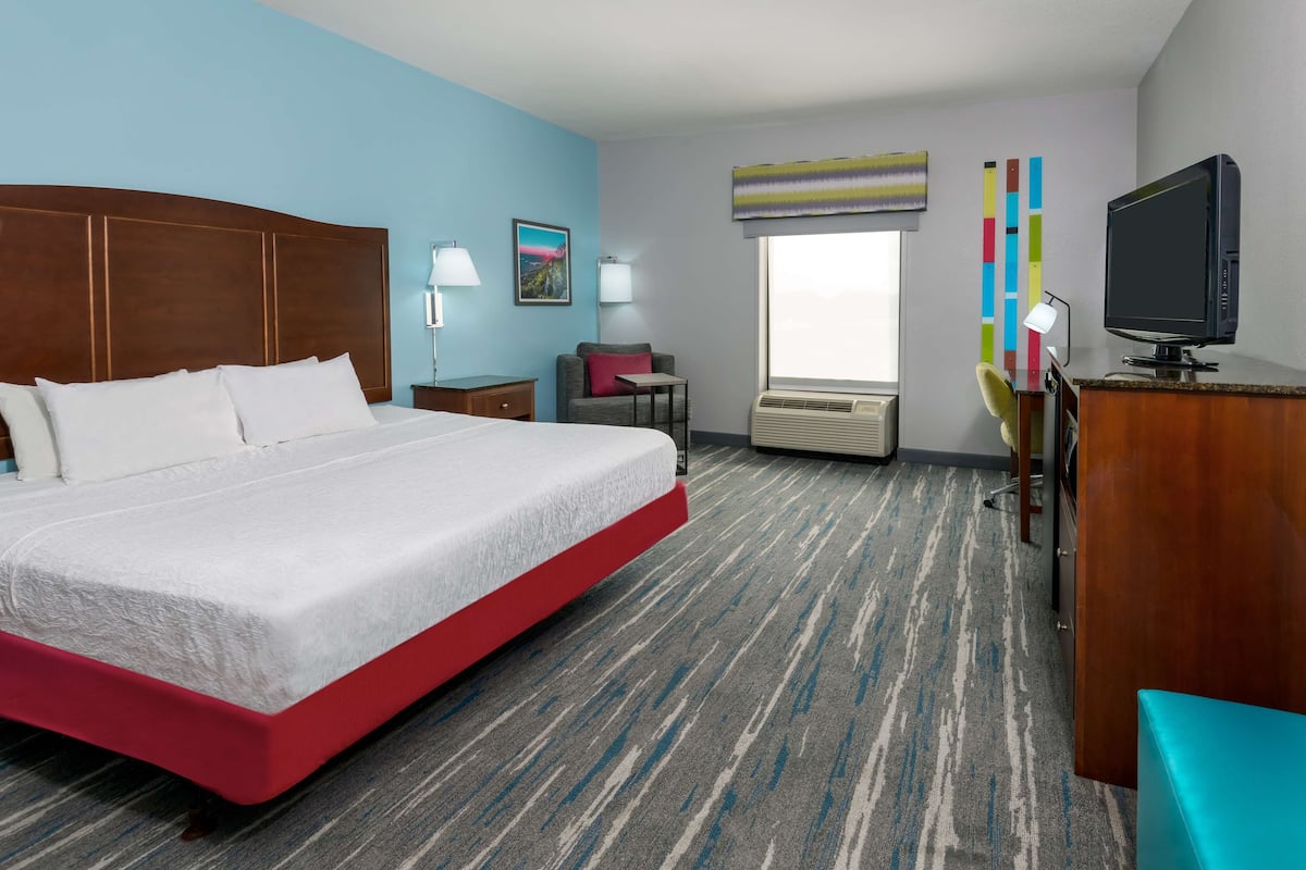 A hotel room with a large bed, a desk, a chair, a TV, and a window with a view.