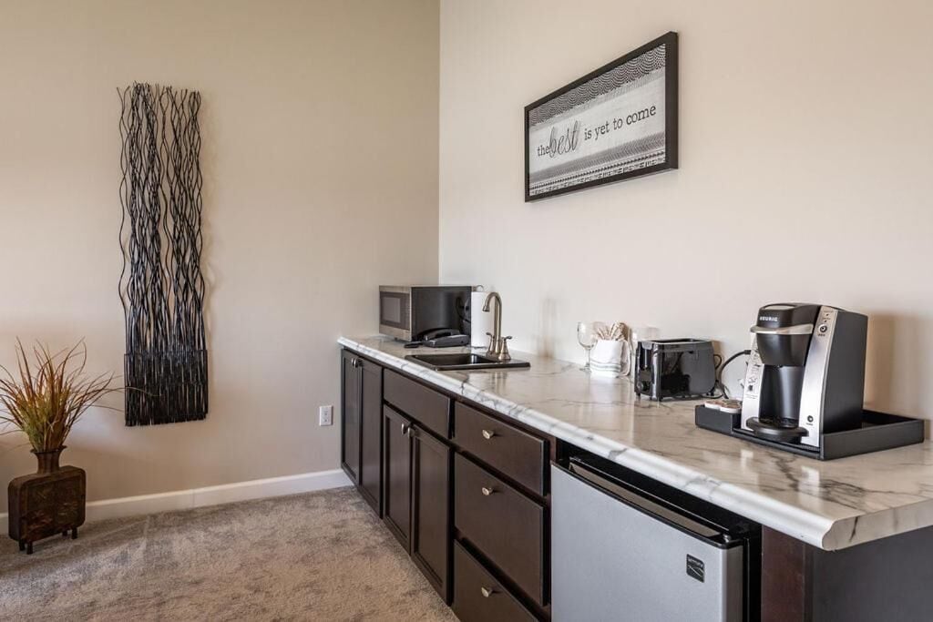 A compact kitchen with dark cabinetry, a marble countertop, a coffee maker, and a framed quote on the wall.