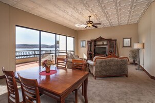 A spacious living room with a large window, a ceiling fan, a dining table with chairs, a sofa, and a television.
