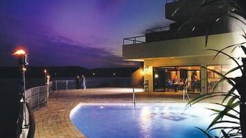 A modern hotel with a pool area, outdoor seating, and a view of the mountains at dusk.