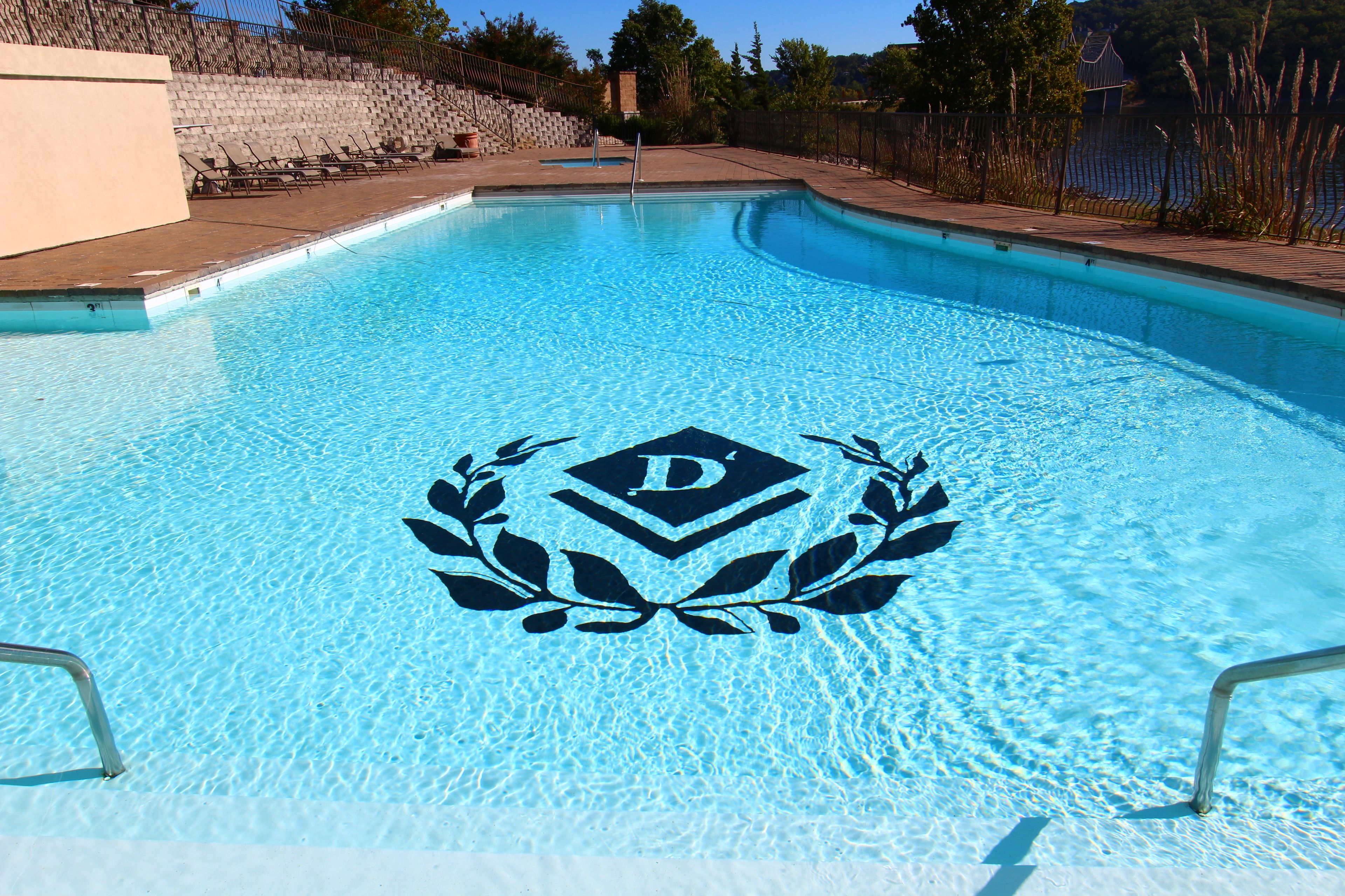 A swimming pool with a logo in the center, surrounded by a stone wall and a fence.