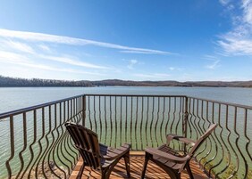 A deck with two chairs and a table overlooking a lake.