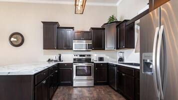 A modern kitchen with dark cabinetry, stainless steel appliances, and a marble countertop.