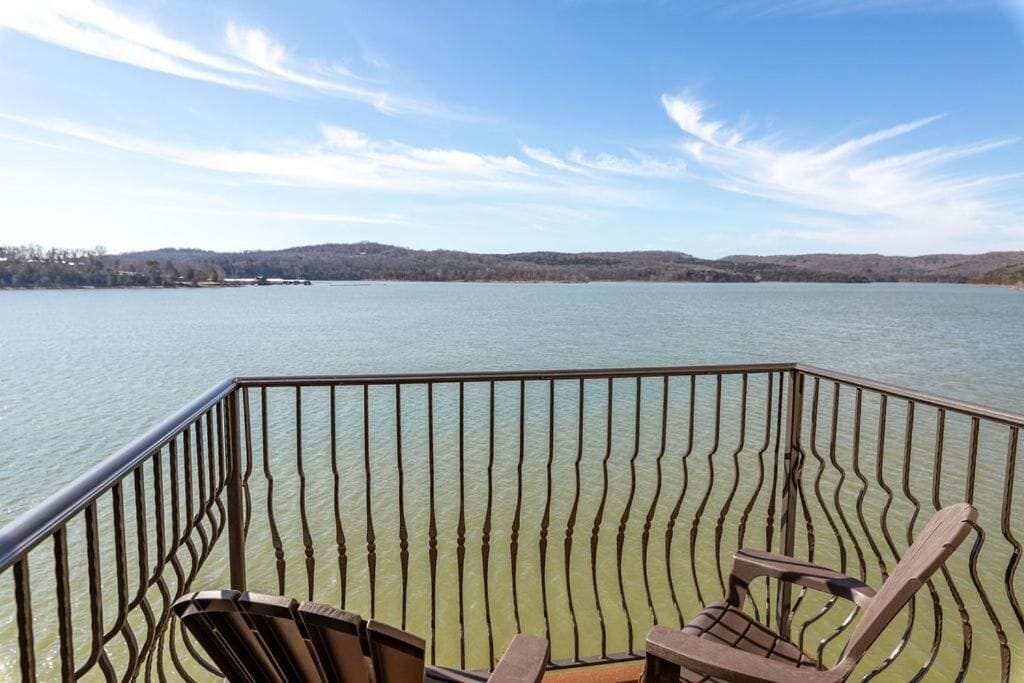 A deck with two wooden chairs and a railing overlooking a calm lake with distant hills.