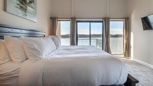Een groot bed met witte lakens in een kamer met uitzicht op een waterpartij vanaf een balkon.
