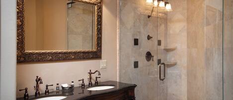 A bathroom with two sinks, a large mirror, and a glass-enclosed shower.