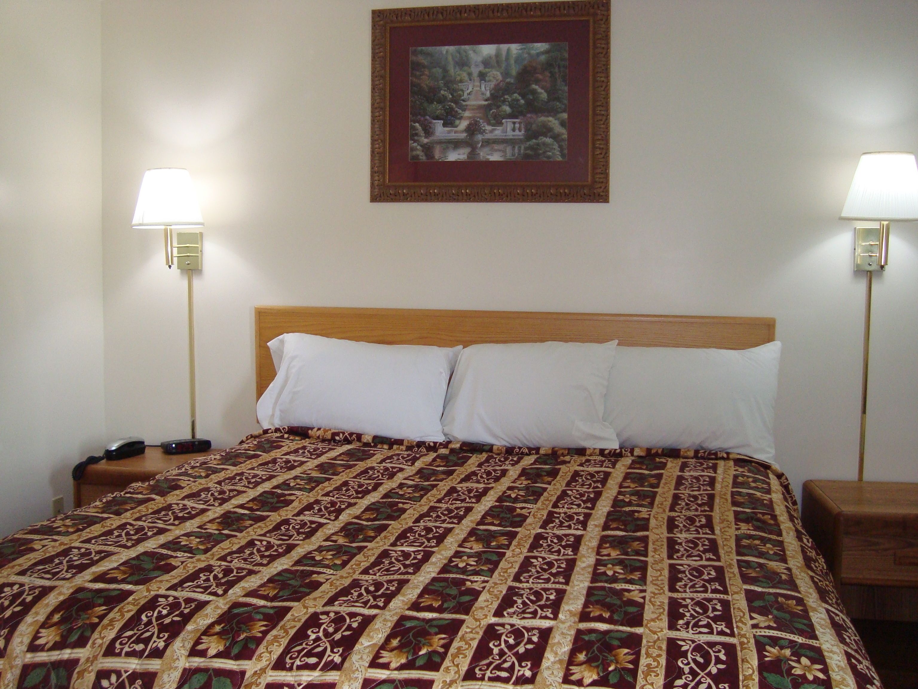 A neatly made bed with a patterned bedspread, two bedside lamps, and a framed picture on the wall.