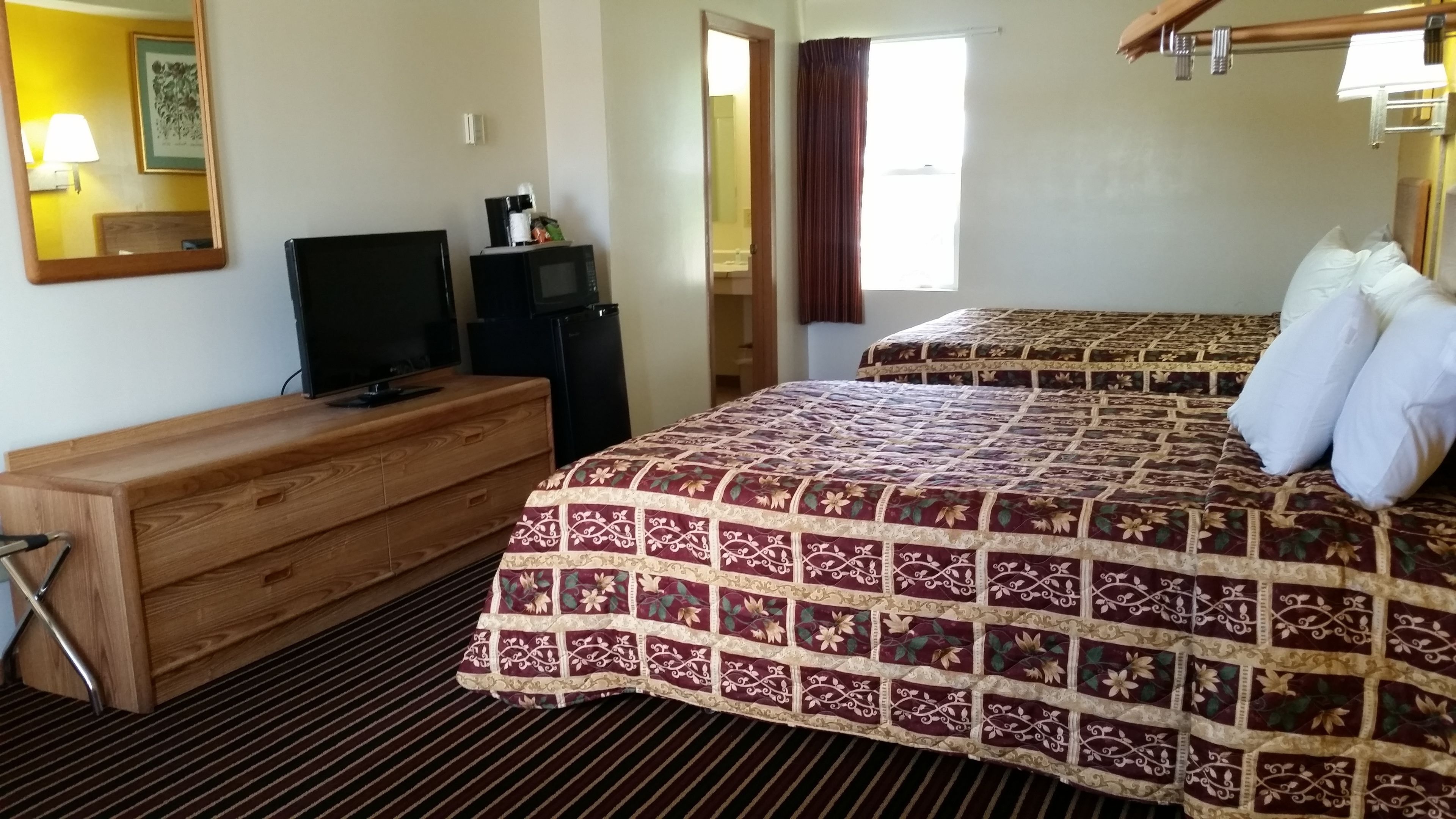 Habitación de hotel con tocador de madera, televisión, dos camas con ropa de cama estampada con motivos florales y alfombra a rayas.