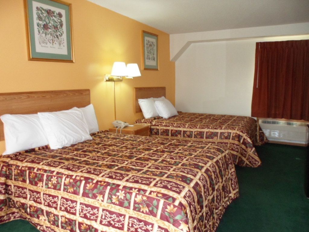 Une chambre d’hôtel avec deux lits, une table de chevet, une lampe et une fenêtre avec des rideaux.