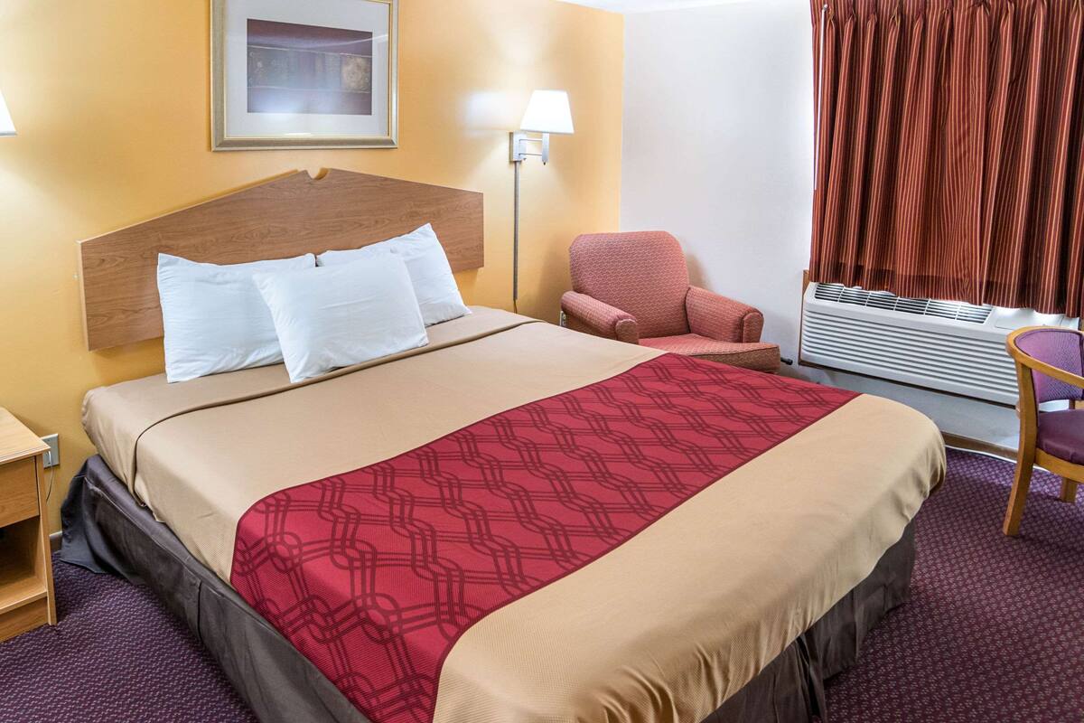 A hotel room with a bed, a chair, a lamp, and a window with curtains.