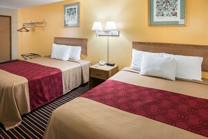 Habitación de hotel con dos camas, una mesita de noche con lámpara, teléfono y perchero.