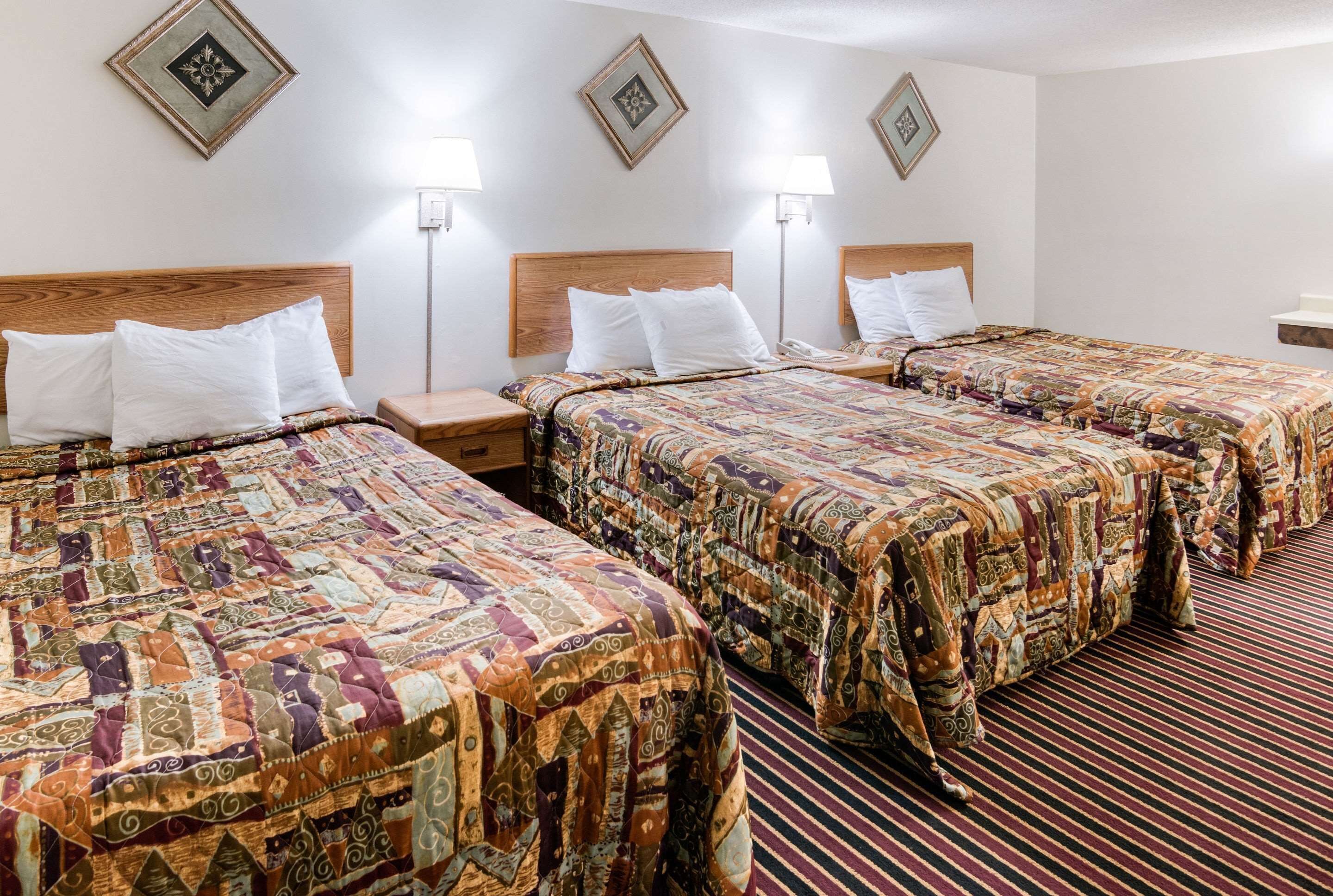 Quarto de hotel com três camas, cada uma com colcha estampada e almofadas brancas. Há luminárias de cabeceira em cada mesa de apoio.
