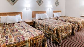 Quarto de hotel com três camas, cada uma com colcha estampada e almofadas brancas. Há luminárias de cabeceira em cada mesa de apoio.