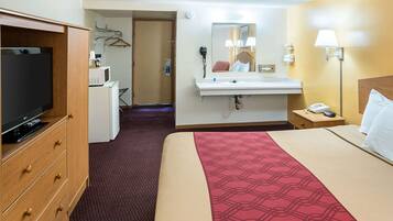 Habitación de hotel con cama, televisión, escritorio con computadora, espejo, lavamanos y lámpara.