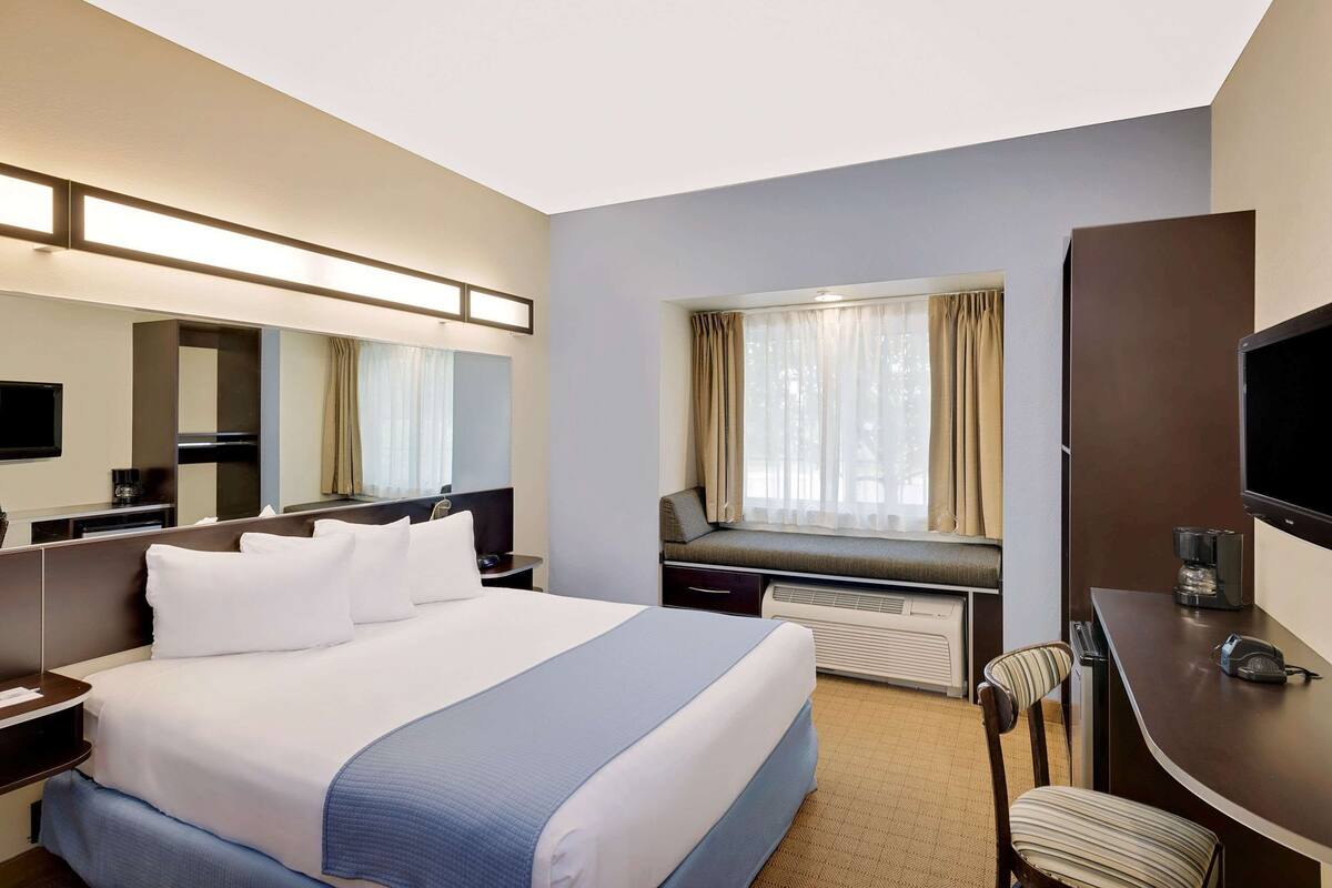 A hotel room with a large bed, a desk, a chair, a television, and a window with curtains.