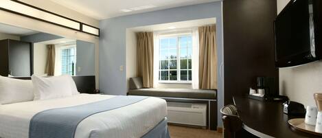 A hotel room with a large bed, a desk with a chair, a flat-screen TV, and a window with curtains.