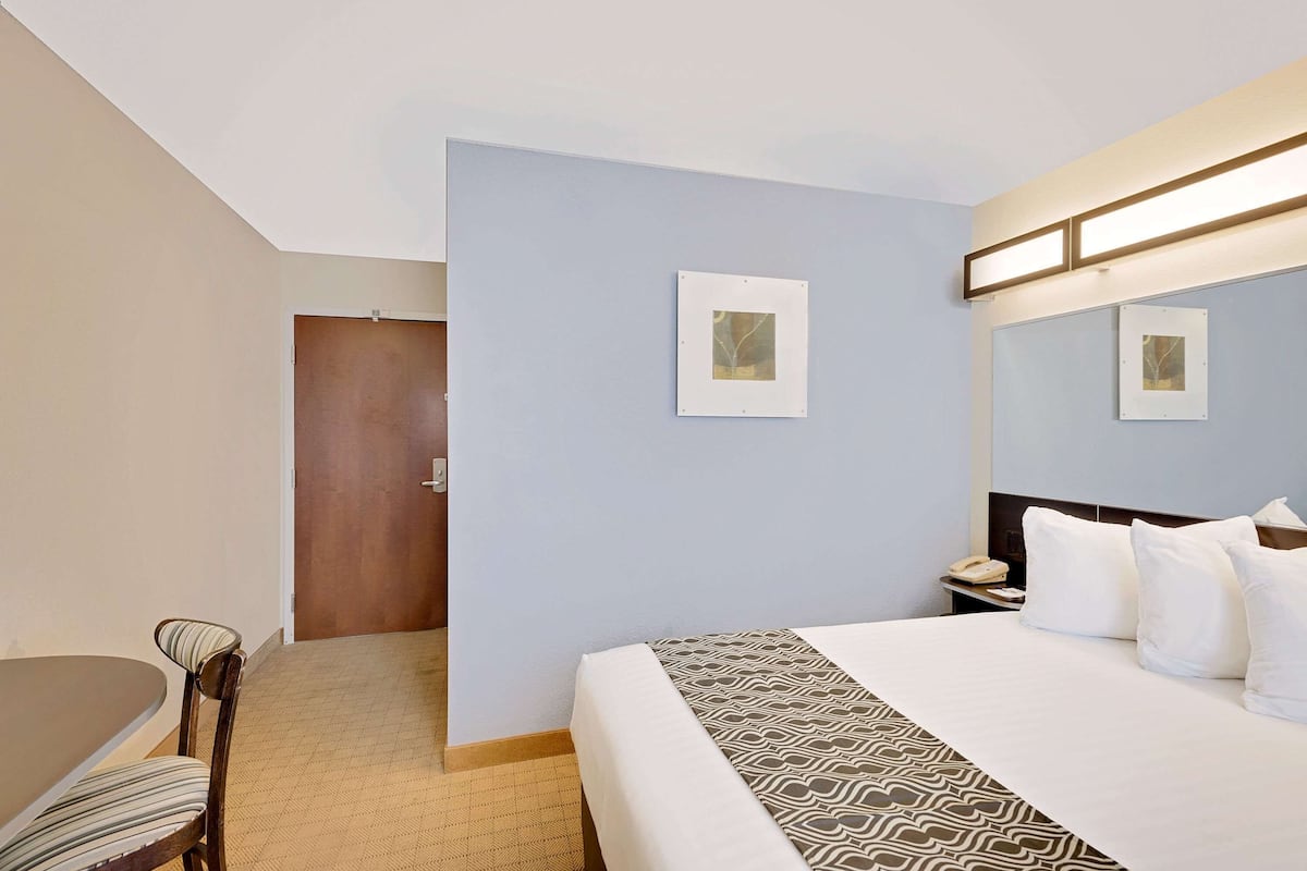 A hotel room with a bed, a desk, and a chair. There are two framed pictures on the wall.