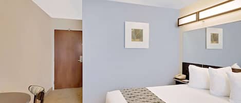 A hotel room with a bed, a desk, and a chair. There are two framed pictures on the wall.