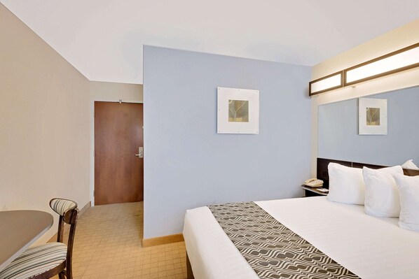 Une chambre d’hôtel avec un lit, un bureau et une chaise. Deux tableaux encadrés sont accrochés au mur.