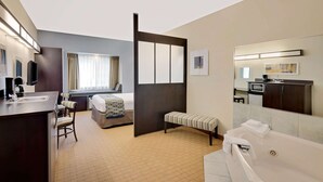 A hotel room with a bed, a desk with a chair, a bench, a bathtub, a mirror, and a TV. - Microtel Inn & Suites by Wyndham Geneva (Geneva)