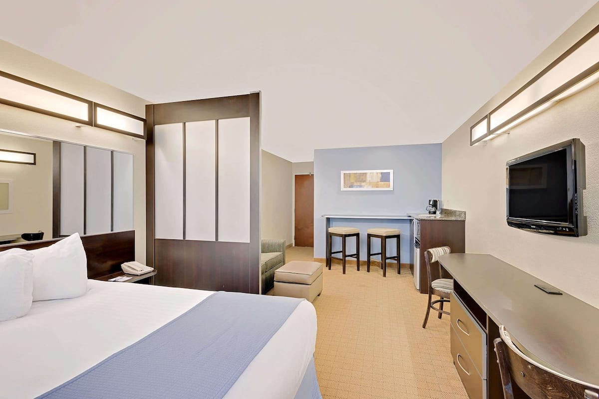 A hotel room with a large bed, a desk with two chairs, a television, and a small kitchenette area.