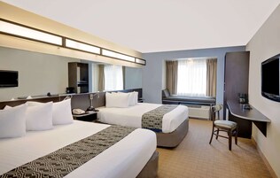 Habitación de hotel con dos camas, un escritorio, una silla, un televisor y una ventana con cortinas.
