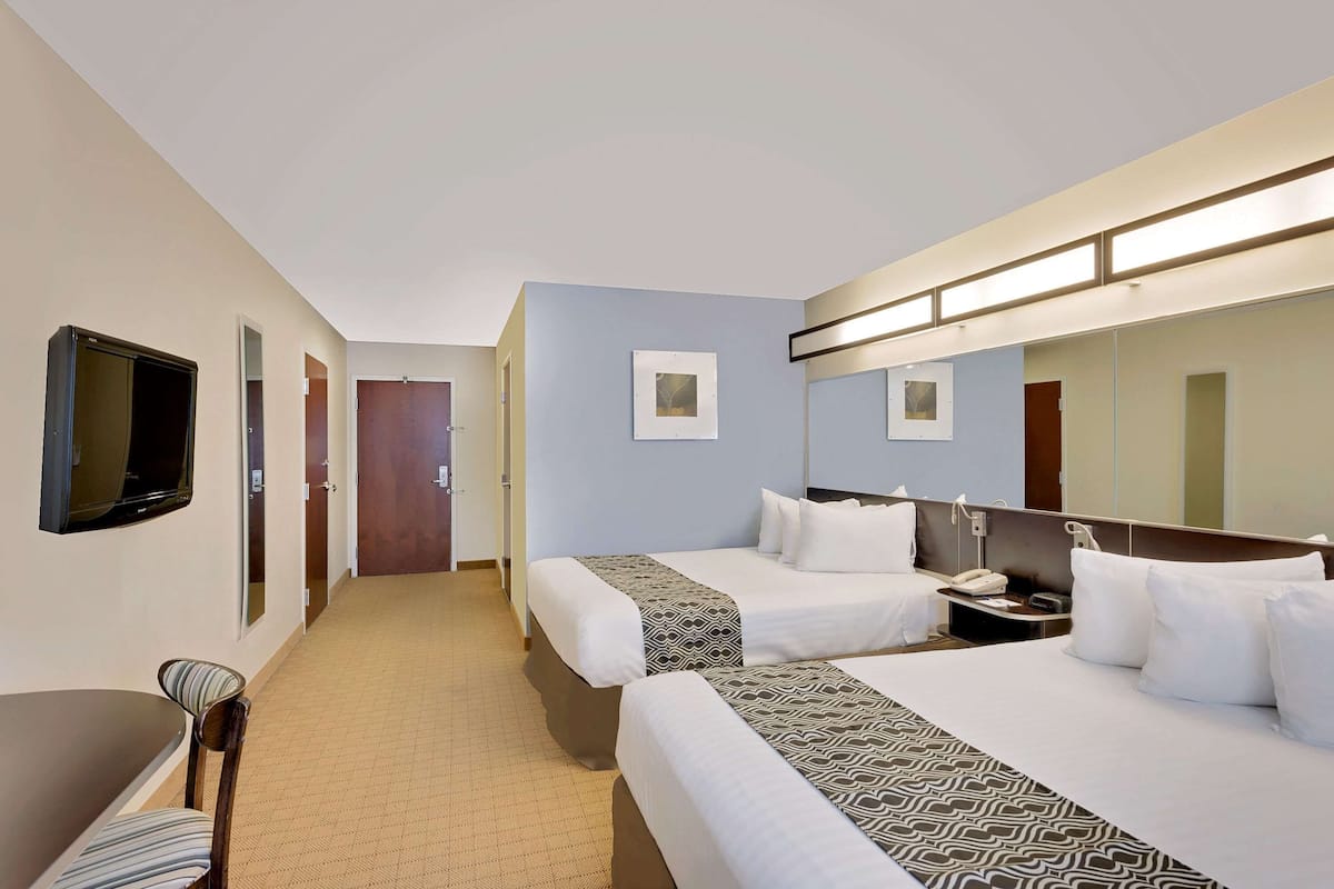A hotel room with two beds, a desk, a chair, a TV, and a mirror.