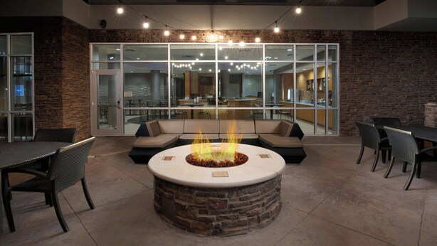A modern outdoor seating area with a stone fire pit, surrounded by wicker furniture and a glass partition. - SpringHill Suites by Marriott San Angelo (San Angelo)