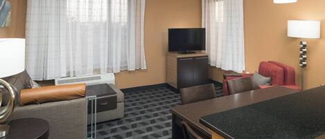 Habitación de hotel con sofá, televisión, mesa de comedor y lámpara.