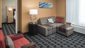 A hotel room with a sofa, armchair, and ottoman, a small side table, a lamp, a painting, and a window with curtains. - TownePlace Suites by Marriott Panama City (Panama City)