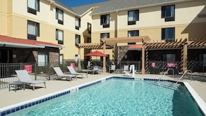 A hotel pool area with lounge chairs and umbrellas, a stone facade, and a clear blue pool. - TownePlace Suites by Marriott Panama City (Panama City)