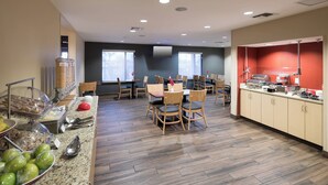 A hotel dining area with a buffet setup, wooden chairs, and a counter with food items. - TownePlace Suites by Marriott Panama City (Panama City)
