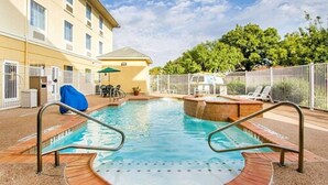 A swimming pool with a circular hot tub area, surrounded by a fence and a building with multiple windows. - Comfort Suites Abilene Central (Abilene)