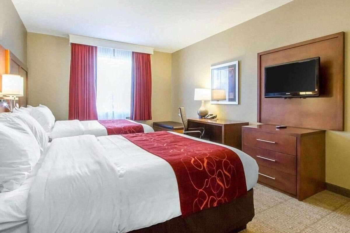 A hotel room with two beds, a desk, a chair, a TV, and a window with curtains.