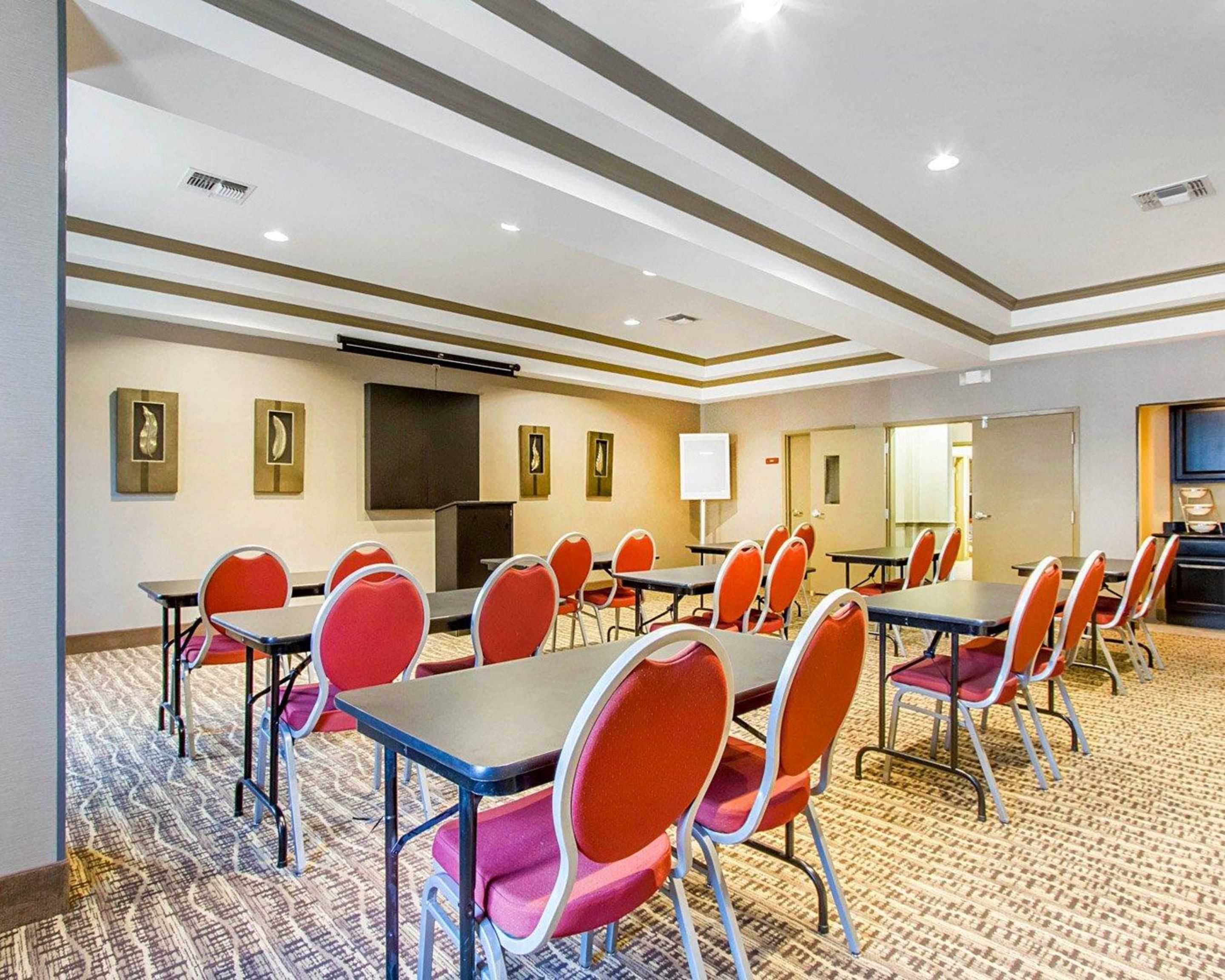 A conference room with multiple tables and chairs, a projector screen, and a large screen on the wall.