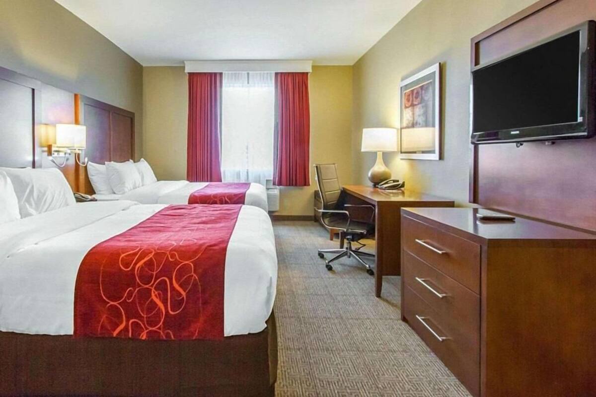 A hotel room with two beds, a desk, a chair, a television, and a window with curtains.