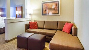 A hotel room with a brown sofa, two red pillows, a floor lamp, and a framed abstract painting on the wall. - Comfort Suites Abilene Central (Abilene)