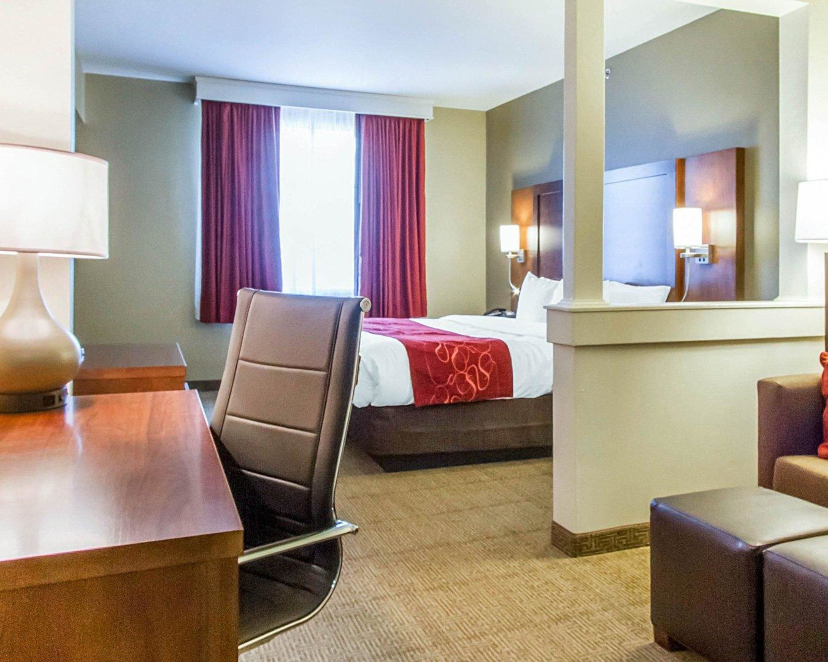 Une chambre d’hôtel avec un lit, un bureau, une chaise, un miroir et une fenêtre avec des rideaux.