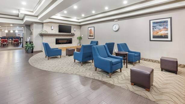 A lobby with a fireplace, blue armchairs, a clock, and a television on the wall. - Comfort Suites Abilene Central (Abilene)